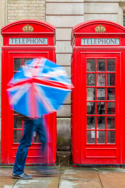 Red London Telephone boxes in the rain with a person holding a Union Jack Umbrella London England UK