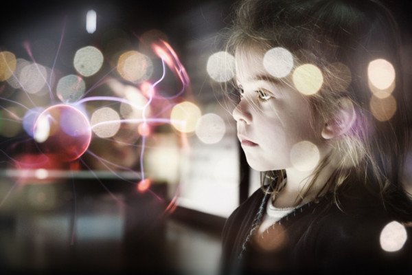 A small female child looking at a plasma ball