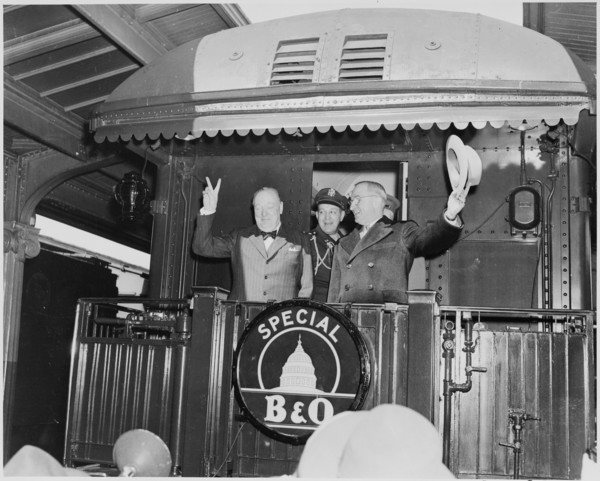 Photograph of President Truman waving his hat and Winston Churchill flashing his famous V for Victory sign from the rear platform of a special Baltimore & Ohio train (evidently en route to Fulton, Mis...
