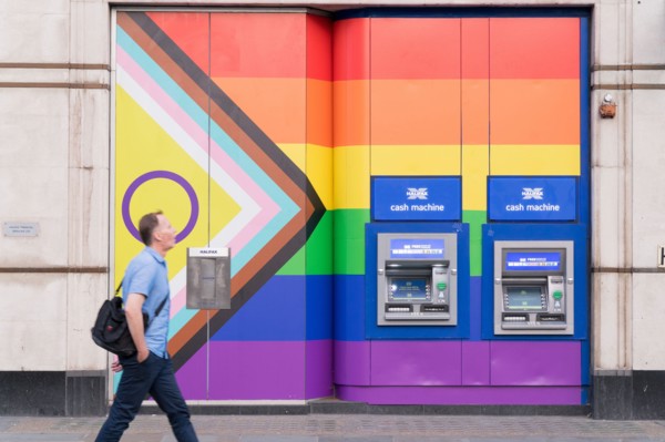 A man walks past two cash machines on the wall painted with rainbow colours during celebration of Pride Month England UK