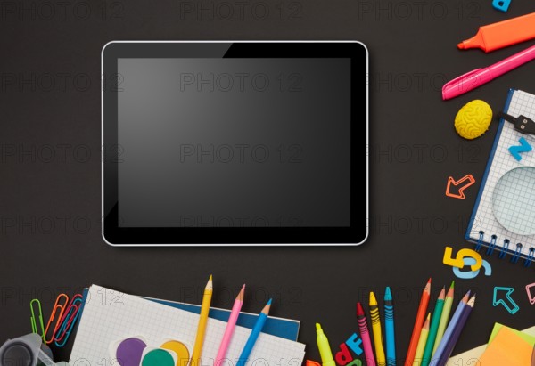 Digital tablet and school supplies on blackboard