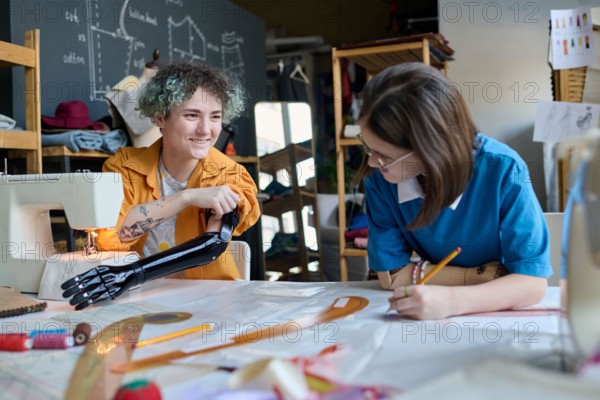 Portrait of two smiling teenage girls with prosthetics sewing clothing together in inclusive training class