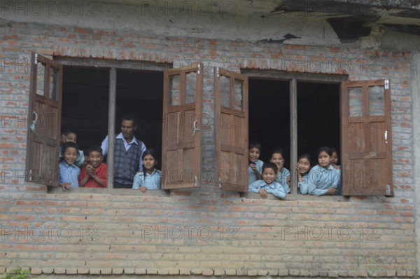 Nepalese children looking out of their classroom 's window together with their teacher curious for who is in their non touristy small village, Panauti.