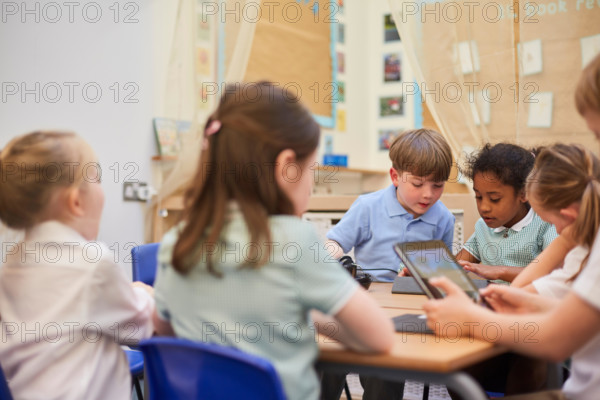 Schoolboys and girls looking at digital tablets in class at primary school