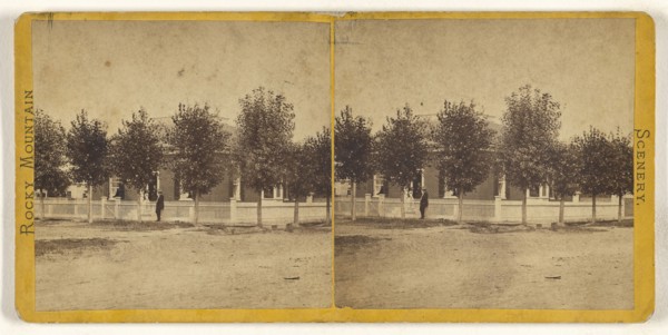 Rocky Mountain Scenery. Man in hat standing in front of a large tree-lined house, with white picket fence; American; about 1870