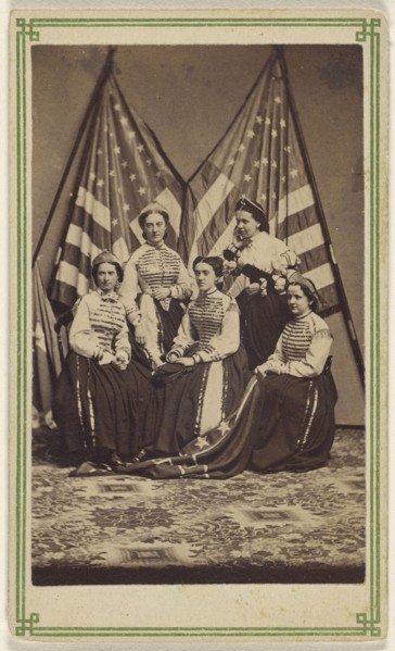 Five women, two standing, three seated, in costume, posed in front of two American flags; American; about 1865; Albumen silver