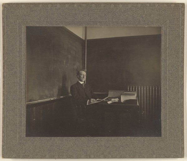 Portrait of a male teacher seated at his classroom desk; American; about 1900; Gelatin silver print