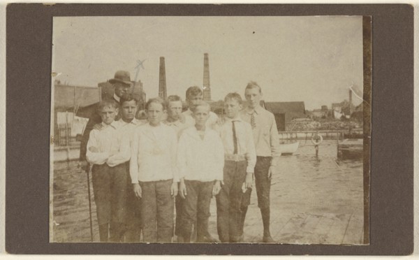 Eight young men standing on a dock near a river, with a man wearing a hat; 1875 - 1885; Albumen silver print