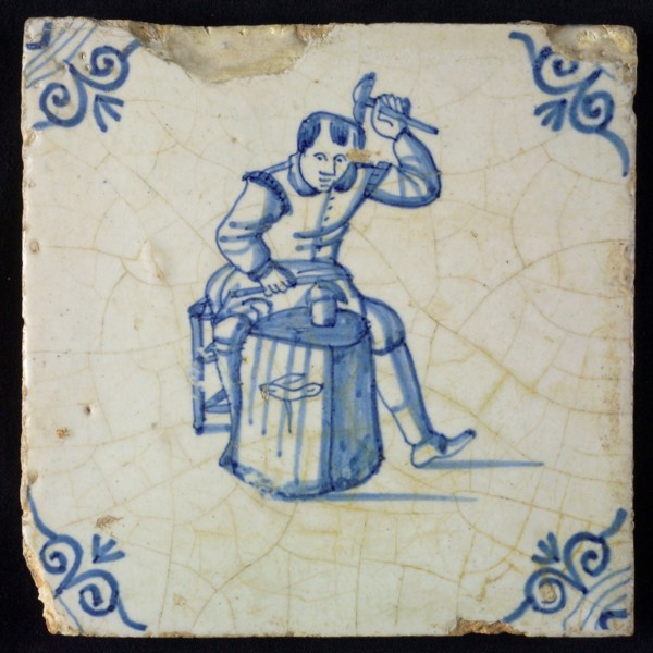 Occupation tile, blue with seated blacksmith with raised hammer and anvil, corner motif oxen head, wall tile tile sculpture