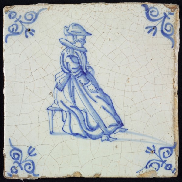 Figure tile, blue with lady sitting on stool, with hat, wide collar and apron, corner pattern ox head, wall tile tile sculpture