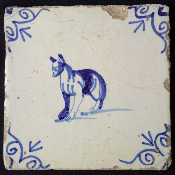 Animal tile, standing dog to the left with strange legs, in blue on white, corner motif ox's head, wall tile tile sculpture