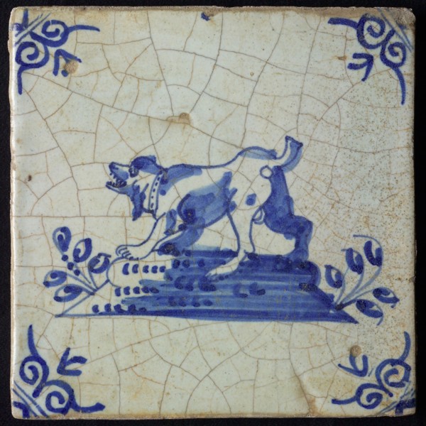 Animal tile, barking standing dog to the left on plot, in blue on white, corner motif oxen head, wall tile tile sculpture