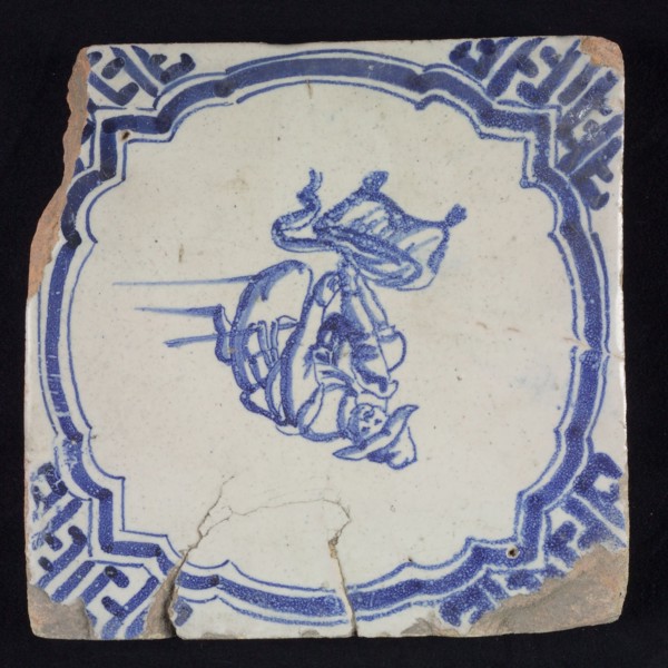 Figure tile, blue with man on knees, hunter taking something out of his bag, scalloped frame with braces, corner motif meander