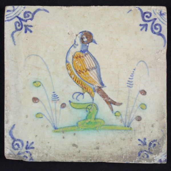 Animal tile, bird on branch to the left in orange, green, brown and blue on white, corner pattern ossenkop, wall tile