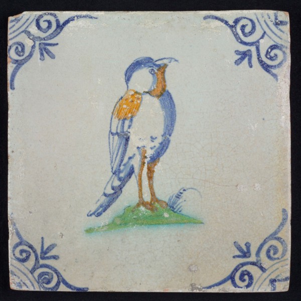 Animal tile, bird with on ground to the right in orange, yellow, green and blue on white, corner pattern ox head, wall tile