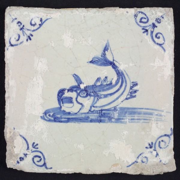Animal tile, unknown fish in water to the left with open beak and curled tail, in blue on white, corner motif steered ox's head
