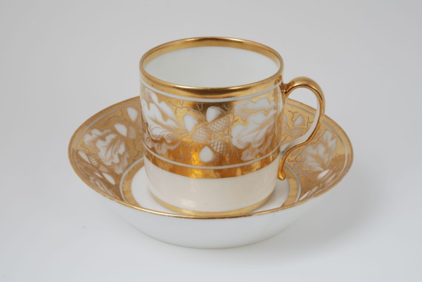 White cup and saucer with gold colored band with acorn and leaf decoration, cup and saucer drinking utensils tableware holder