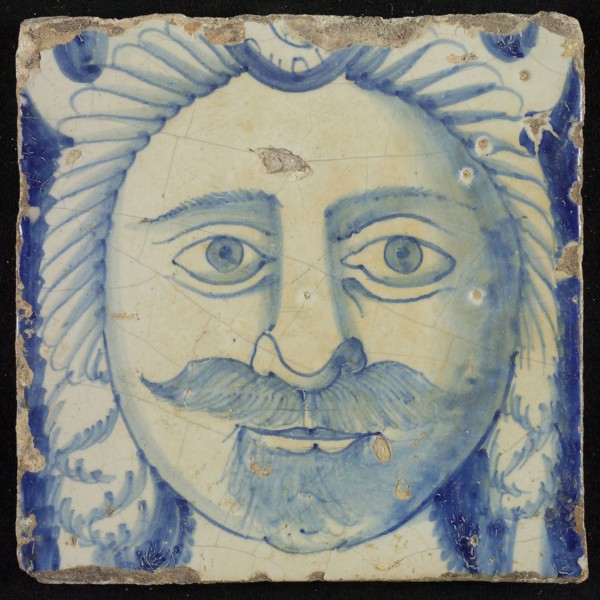 Tile of chimney pilaster, blue on white, head of man with long curly hair and mustache, beginning of shell-shaped headdress