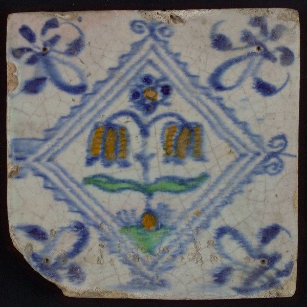 Tile, double flower on ground in orange, green and blue on white, inside serrated square with plume, corner pattern french lily