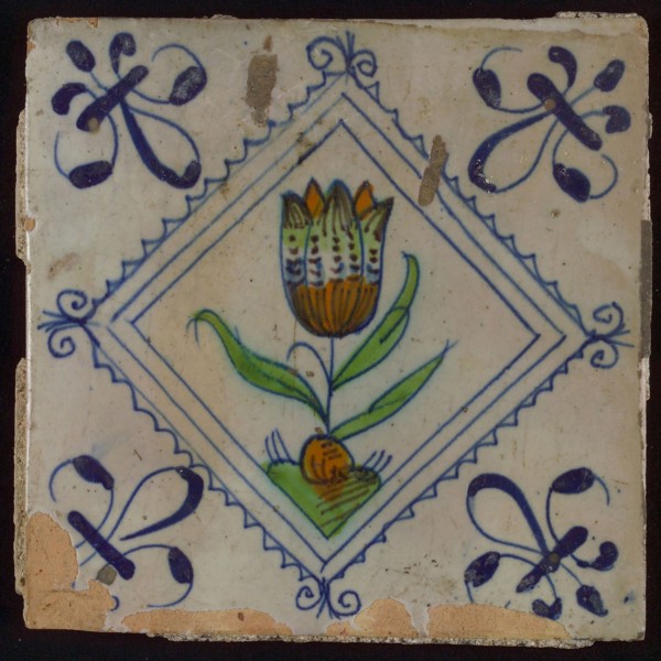 Tile, tulip on ground in orange, brown, green and blue on white, inside serrated square with plume, corner pattern french lily