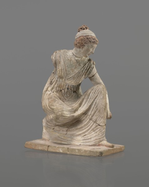 Terracotta figurine of a girl throwing dice. Female figurine of a crouching girl throwing dice;