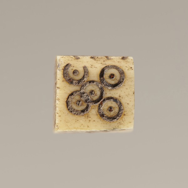 Game die made of animal bone with six unequal sides. Each side is engraved with a number from 1 to
