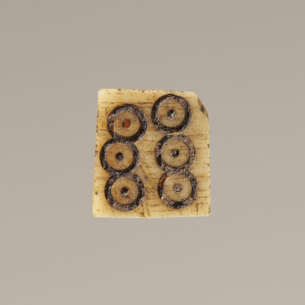 Game die made of animal bone with six unequal sides. Each side is engraved with a number from 1 to