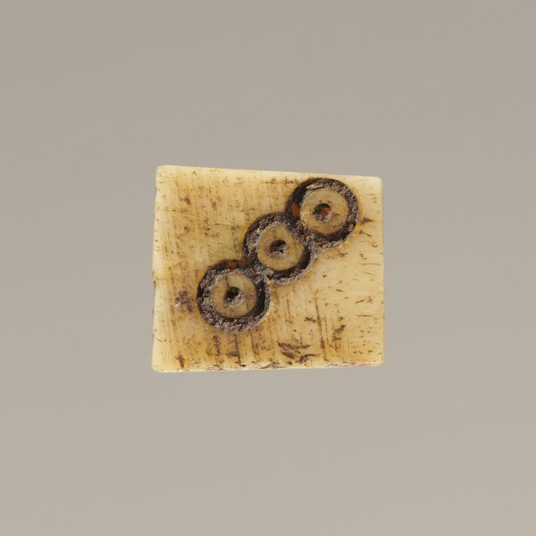 Game die made of animal bone with six unequal sides. Each side is engraved with a number from 1 to
