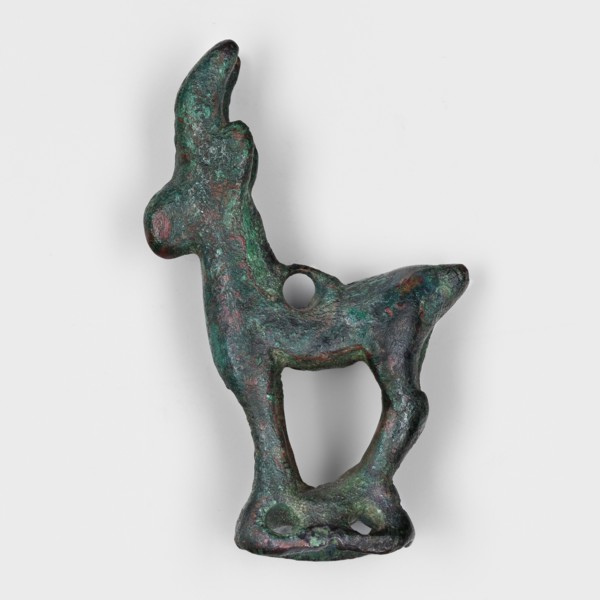 Figurine of an ibex goat standing on a hollow prism base with two pairs of holes on the longer