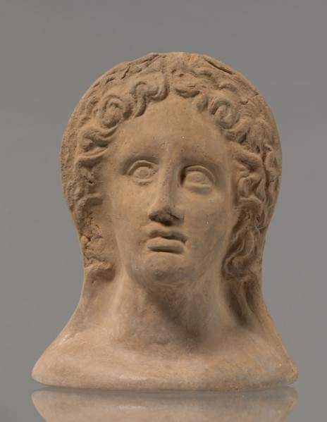 Votive female head, female head wearing a wreath, from under which lush locks of hair curl down the