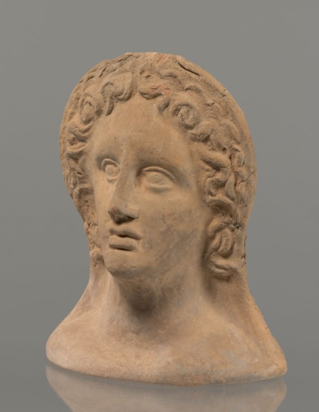 Votive female head, female head wearing a wreath, from under which lush locks of hair curl down the