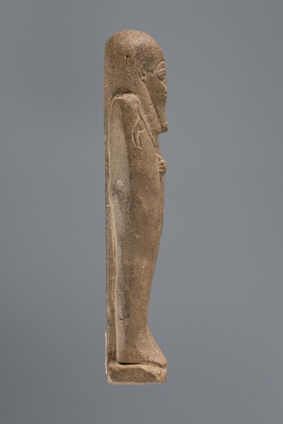 Ushabti, mummy-shaped figurine, standing on a base with a pilaster at the back. Arms crossed on the