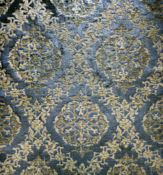 A fabric fragment: a diagonal net of plant and floral tendrils against a blue velvet background. In