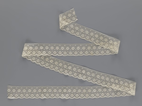Lace fragment tied in the form of a belt with one-sided arched serrations. Regular ornament of