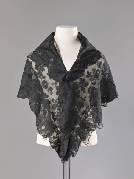 Cape in the form of an elongated rhombus, made of black lace with floral motifs. The edge is