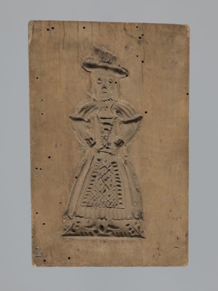 Double-sided gingerbread form. Obverse: female figure in a long patterned dress wearing a hat.