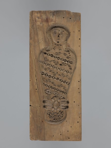 Double-sided gingerbread form. Obverse: female figure in a hat and a long patterned dress. Reverse:
