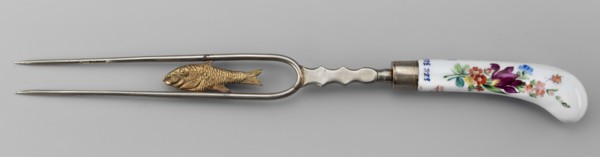 Two-pronged fork with a gilded plastic fish between the tines and a plastic palmette at the base;