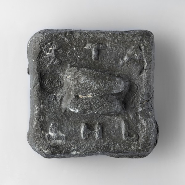 Square weight with diagonally cut side edges. The upper surface is decorated with a plastic