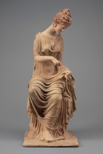 Figurine of a woman sitting on a rock with a flower in her hand. Woman sitting on a rock with a