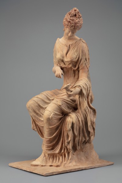 Figurine of a woman sitting on a rock with a flower in her hand. Woman sitting on a rock with a