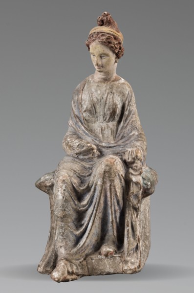 Figurine of a woman. A girl sitting in a chair is dressed in a soft white chiton over which a blue,
