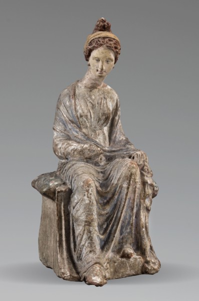 Figurine of a woman. A girl sitting in a chair is dressed in a soft white chiton over which a blue,