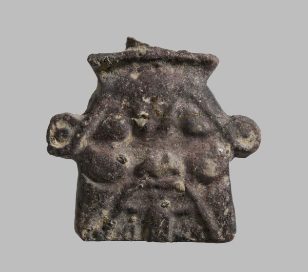 Plaque with a schematic relief representation of the head of Bes. The crown has been knocked off,