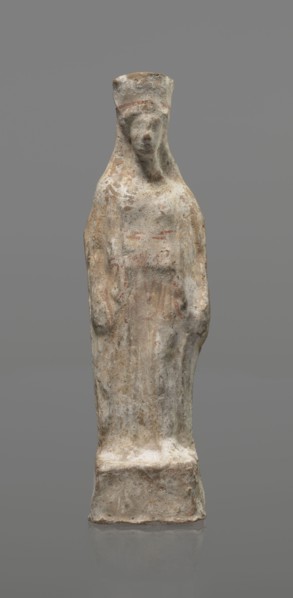 Female terracotta figurine of a standing woman, depicted frontally. Set on a small hollow,