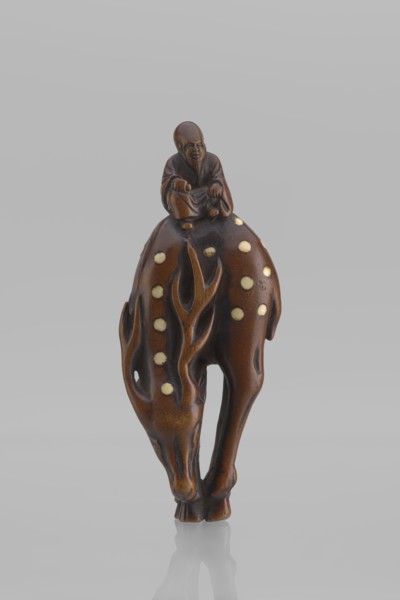 Netsuke in the shape of Fukurokuju riding a deer. The deer has all its legs put together so that