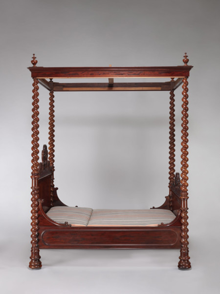 Four-poster double bed with flat pediments topped with a wavy pattern, framed by tall spiral