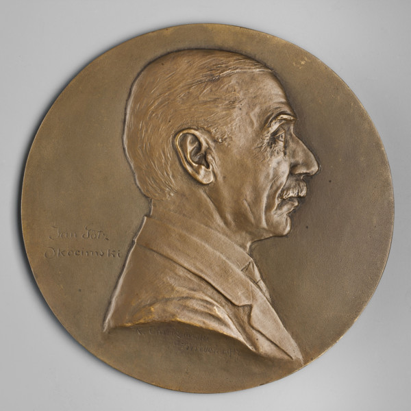 Bust of a man in right profile, hair smoothly combed back, mustache trimmed, jacket on the