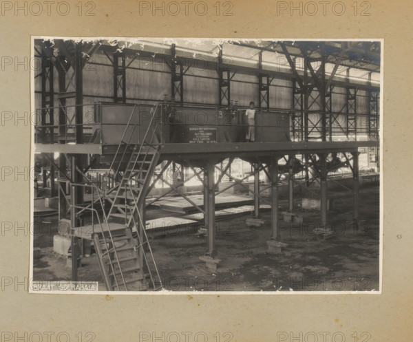 Platform with cooking pots, photograph, Album page with a photo of the interior of a factory hall