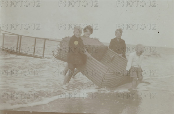 Koosje, Daan and Ben Ochse and another boy carrying a wicker beach chair out of the sea,